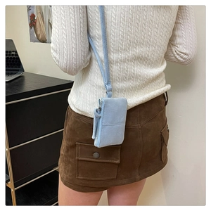 Side view of small blue suede crossbody bag with zipper detail worn with a sweater