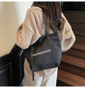 Gros plan d'un grand sac fourre-tout noir en toile avec lettrage blanc sur l'épaule