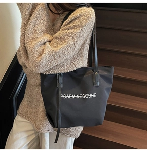 Détail du sac cabas en toile noire montrant le tissu robuste et les coutures de la bandoulière