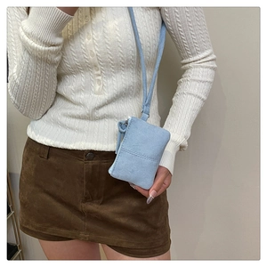 Close-up of a light blue suede mini crossbody bag worn by a model in a minimal outfit