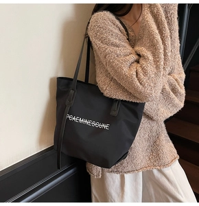Sac fourre-tout noir en nylon grande capacité porté à l'épaule avec inscription blanche