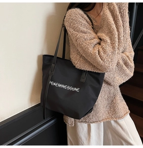 Détail d'un grand cabas noir avec texte blanc porté sur un pull en maille beige