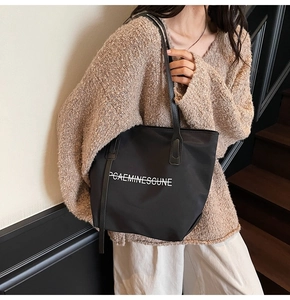 Vue latérale du cabas en nylon noir avec lettrage blanc sur un pull en maille beige