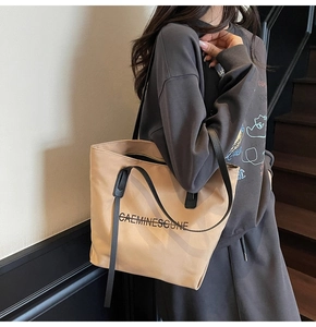 Vue latérale d'un mannequin portant un grand sac cabas en toile marron clair avec logo noir