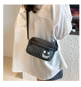 Detail of crossbody bag with vintage monogram pattern and star-eyed smiley face graffiti