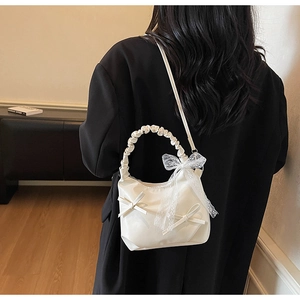 Close-up of creamy white crossbody bag featuring a lace bow and ruched handle detail
