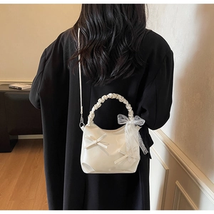 Detail view of white pleated cloud bag with lace bow ribbon on model in black suit