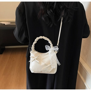 Detail of a creamy white bow cloud bag with pleated handles on a black wool coat