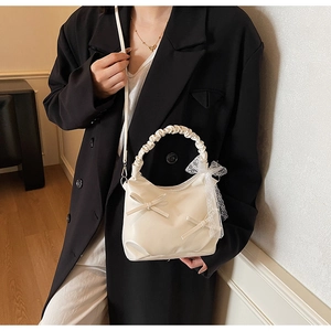 Detail of cream pleated bow handbag with lace charm on a black blazer outfit