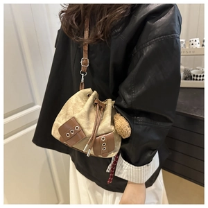 Detailed shot of canvas bucket bag with adjustable brown strap and decorative plush ball