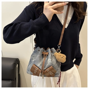 Detail view of denim bucket bag with leather trim and cute brown plush bear charm