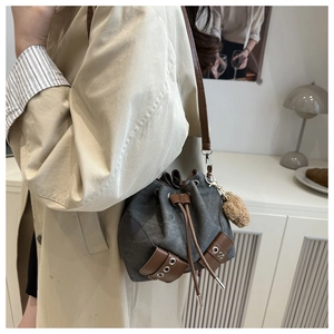 Close-up of drawstring bucket bag in grey canvas with brown leather trim and plush pendant
