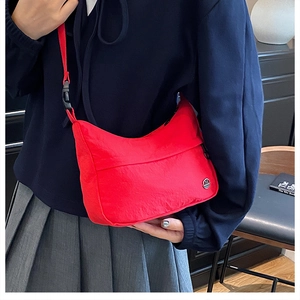 Detail of red nylon crossbody bag with metal logo and adjustable strap on a model