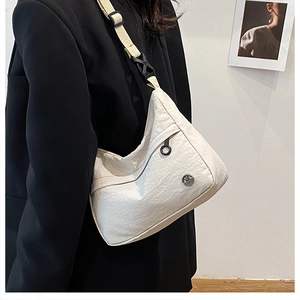 Close-up of white pleated dumpling bag featuring a metal logo and durable nylon strap