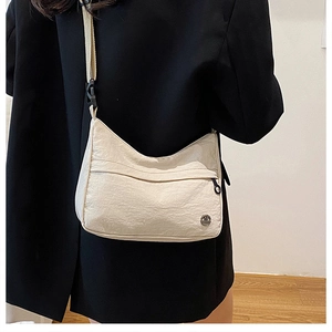 Detail of a cream nylon crossbody bag with silver logo worn over a black blazer