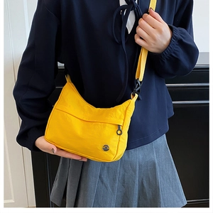 Detail of yellow nylon crossbody dumpling bag featuring a round metal logo and shoulder strap