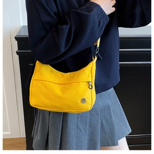 Detail of a bright yellow nylon crossbody bag with adjustable strap and metal logo