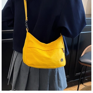 Detail of yellow nylon crossbody bag with adjustable strap and metal logo on a model
