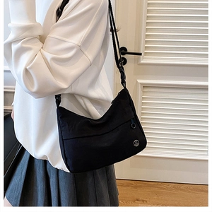 Detail of minimalist black nylon crescent crossbody bag featuring a round metallic logo charm