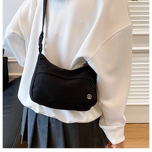 Detail view of the black nylon crossbody bag featuring a metal M logo and wide shoulder strap
