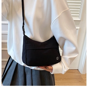 Close-up of black nylon hobo bag featuring a round metal logo and adjustable strap