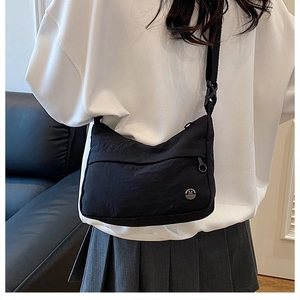 Close-up of black nylon crossbody bag with adjustable strap and M logo on model