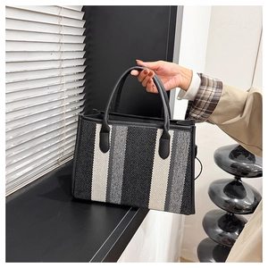 Detail of a large striped tote bag with woven texture and premium black leather handles