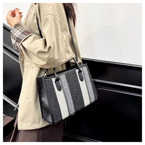 Close-up of a striped tote bag with leather trim and woven texture on a model