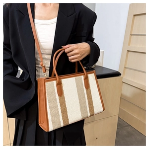 Detail of striped canvas tote bag with brown leather trim and adjustable shoulder strap
