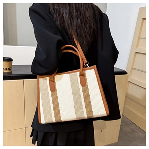 Detail view of woven striped tote bag with brown leather handles worn by a model