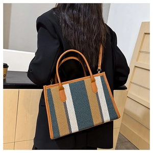 Detail of a large vertical striped tote bag with brown leather handles and vintage style