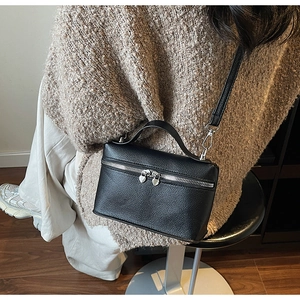 Détail du sac boîte en cuir grainé noir porté avec un pull en maille marron sur l'épaule