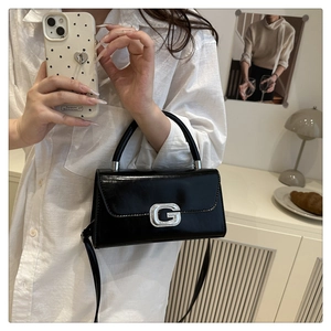 Detail shot of black glossy leather handbag featuring a silver rhinestone encrusted G logo