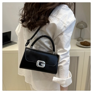 Detail of glossy black leather handbag featuring a crystal-inlaid square metal G-buckle