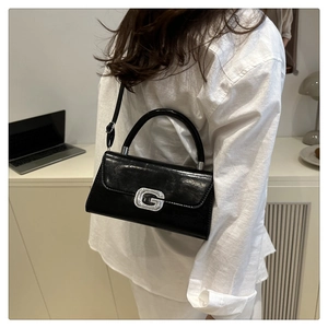 Detail of glossy black handbag with silver rhinestone G-shaped buckle and fine strap