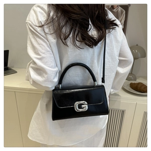 Detail of a black leather crossbody bag with a shiny rhinestone G buckle on a female model