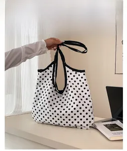 Close-up of canvas tote bag featuring black polka dots and reinforced black stitching detail