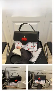 Detail of a chic crossbody bag with red cherry prints and a black flap lid for women