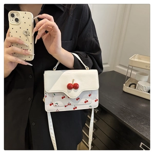 Detail of white cherry print handbag featuring 3D red cherry clasp and leather strap