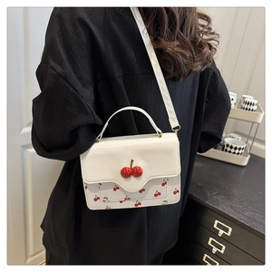 Detailed view of white crossbody bag with red cherry prints and decorative cherry charm