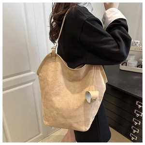 Detail view of large beige suede tote bag with heart charm accessory on shoulder