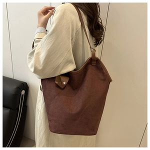 Detail of dark brown suede tote bag with leather trim on model in a modern interior