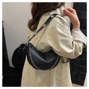 Close-up of black PU leather crescent bag with silver eyelets and chain on shoulder
