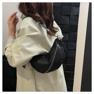 Close-up of black crescent underarm bag with silver chain on model in trench coat
