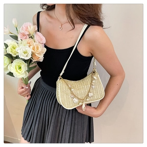 Detail of straw woven underarm bag featuring golden chain and shell pearl charms