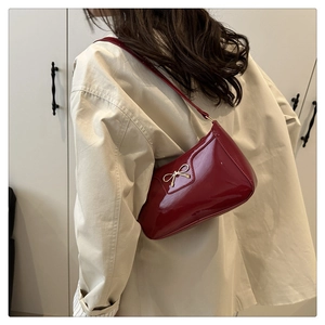 Detail of red patent leather shoulder bag featuring a golden bow metal accessory