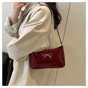 Glossy red faux leather shoulder bag with a gold bow accent worn by a model in a trench coat