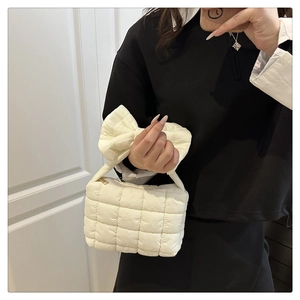 Close-up of white quilted puffer handbag featuring a large bow and soft square texture