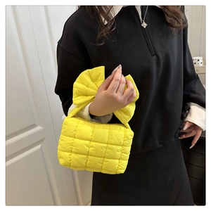 Detail of a bright yellow quilted handbag featuring a large stylish bow on the handle