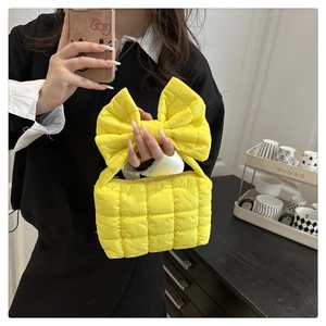 Detail of yellow quilted handbag with large bow and soft polyester square pattern